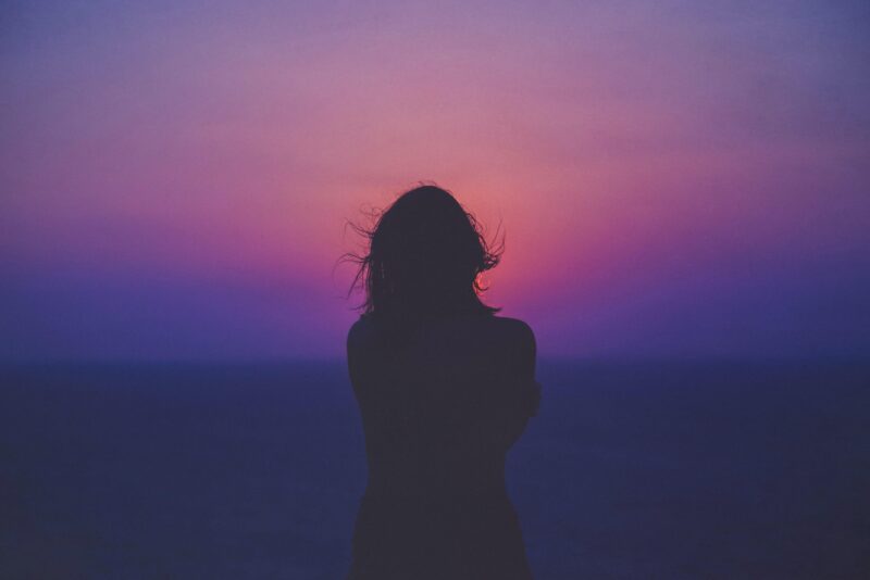 A back of a woman, who is staring into the sunset