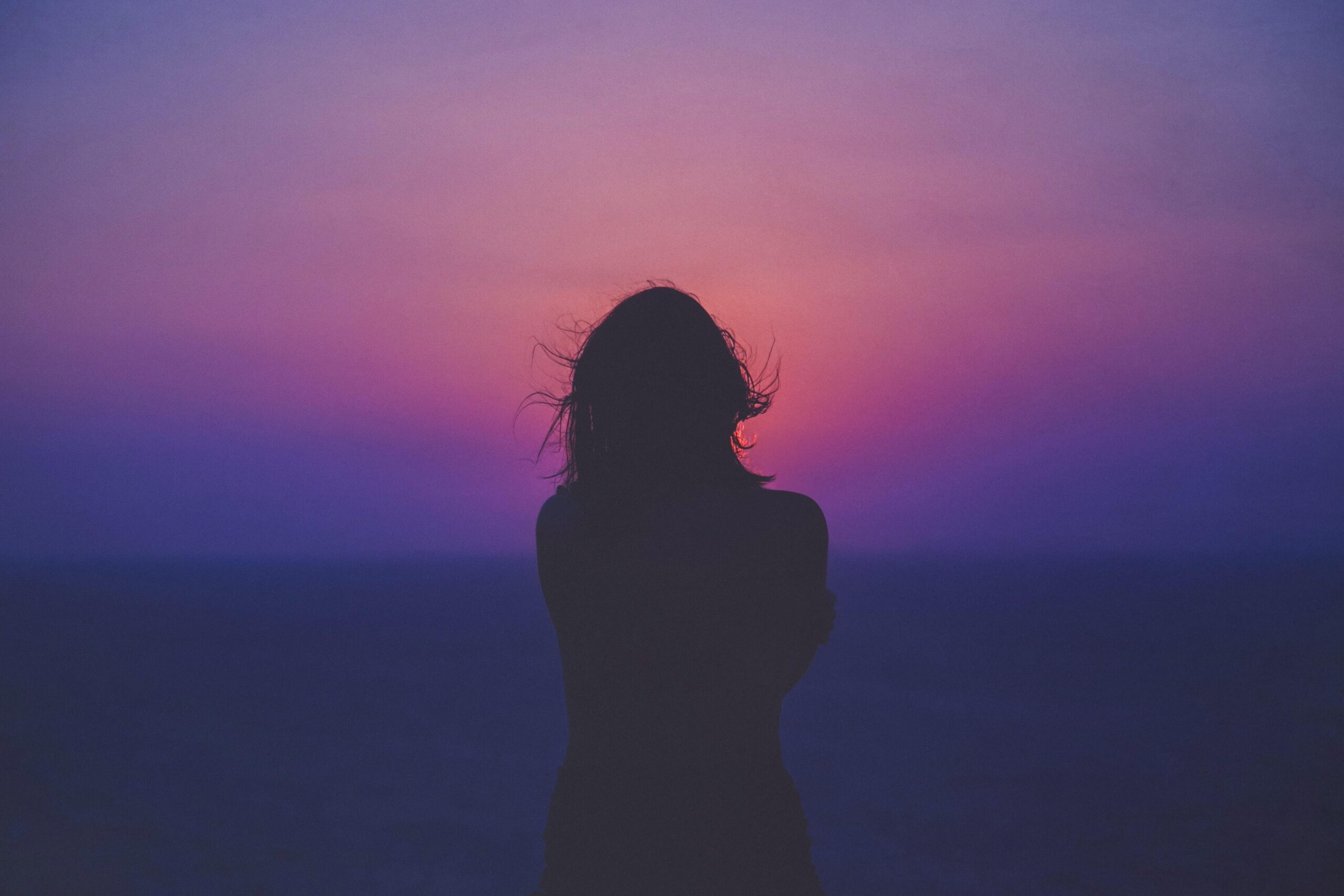 A back of a woman, who is staring into the sunset