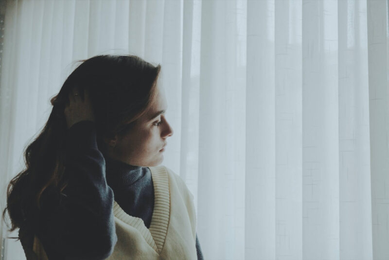 A woman staring outside through the curtains